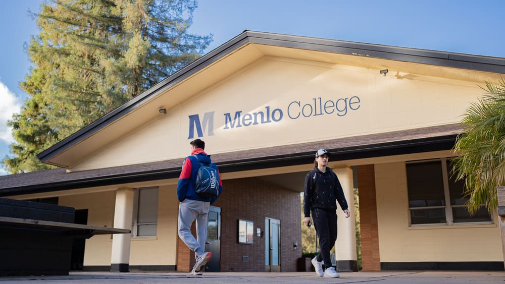 Menlo College sign across an A-frame designed building with students walking in front of it